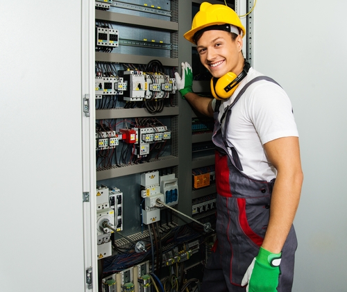 Vrolijke Elektricien In Een Veiligheidsmuts Op Een Fabriek.