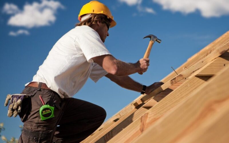 een man met een gele helm werkt in de bouw en is een dak aan het timmeren.