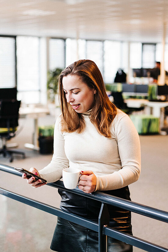 Vrouw bekijkt haar telefoon met een kopkoffie