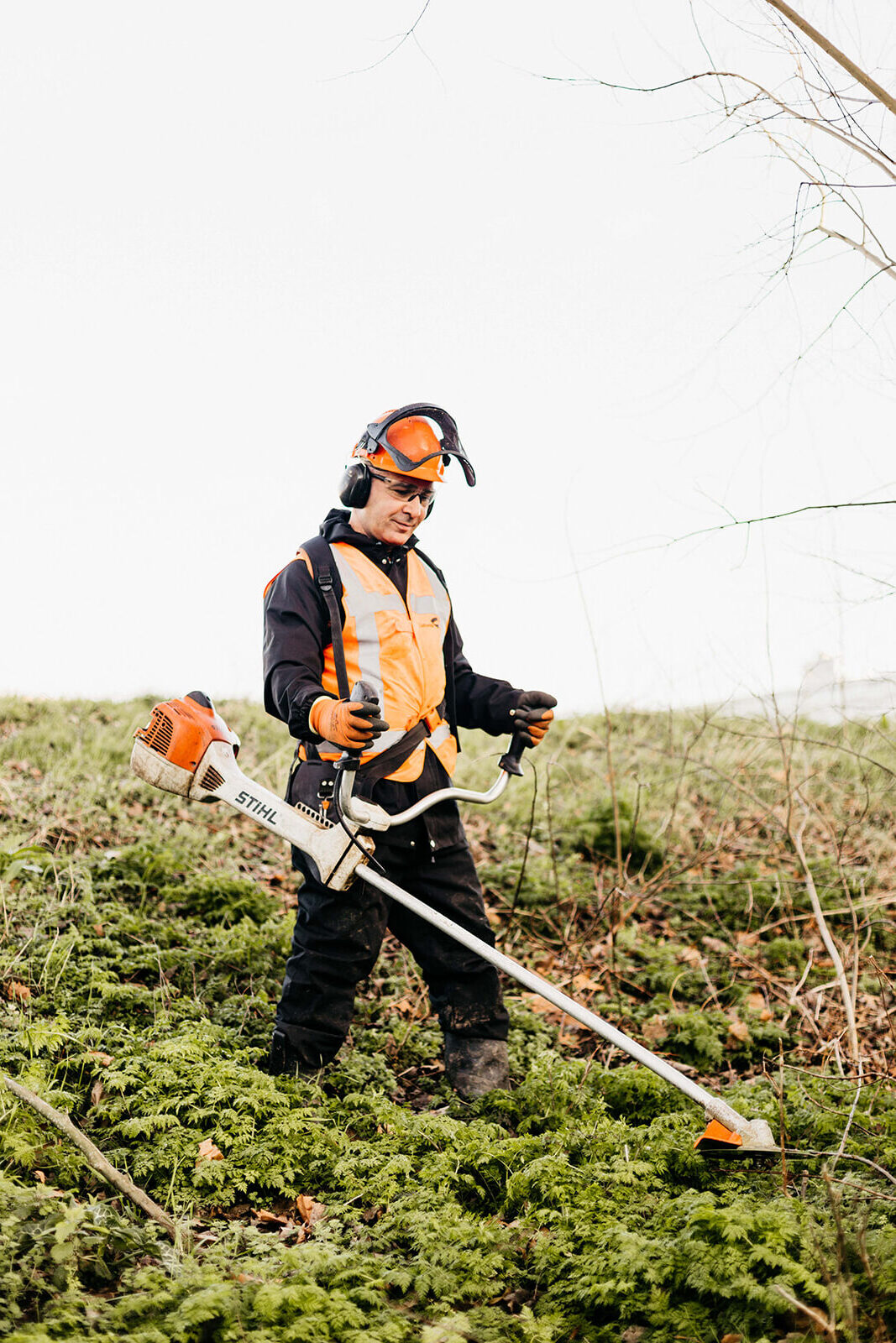 Man is met een snoeimachine de bladeren aan het snoeien. Hij draagt een oranje helm