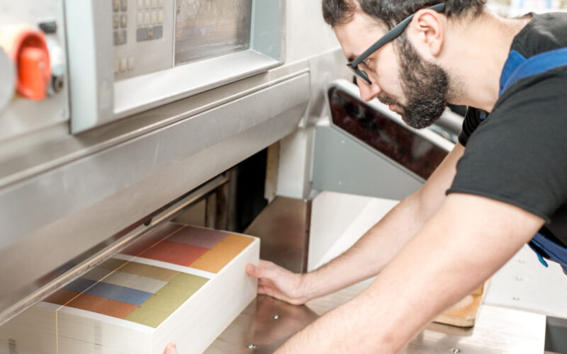 een man die bezig is met zijn werkzaamheden. hij snijdt papier onder een machine