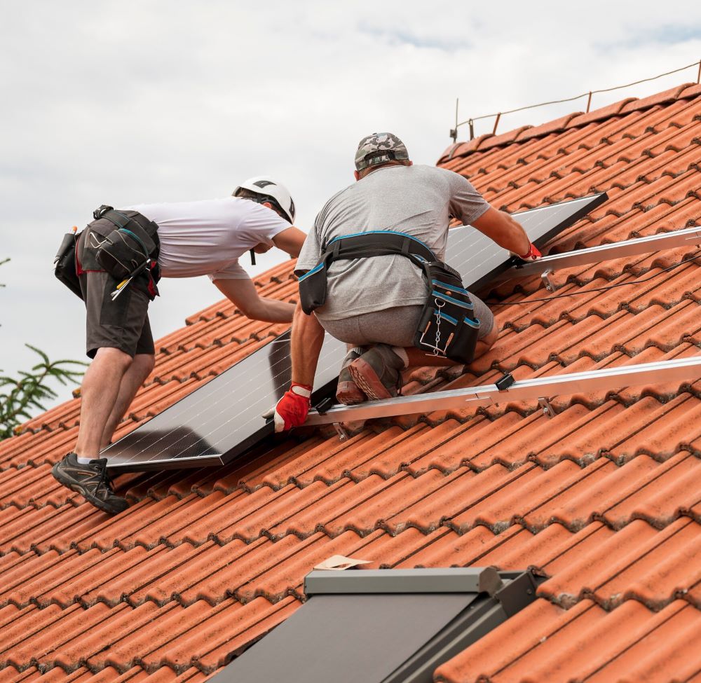een zonnepanelen monteur die bezig is met zijn werkzaamheden op het dak.