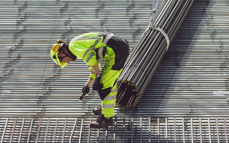 Een medewerker die stalen buizen aan het neerleggen is als voorbereiding van het cement.
