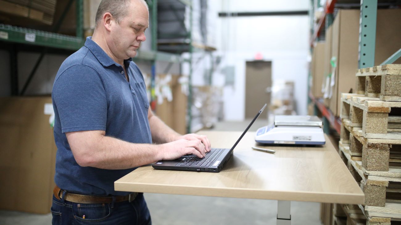 Een werkvoorbereider die achter zijn laptop in een magazijn de bestellingen controleert.