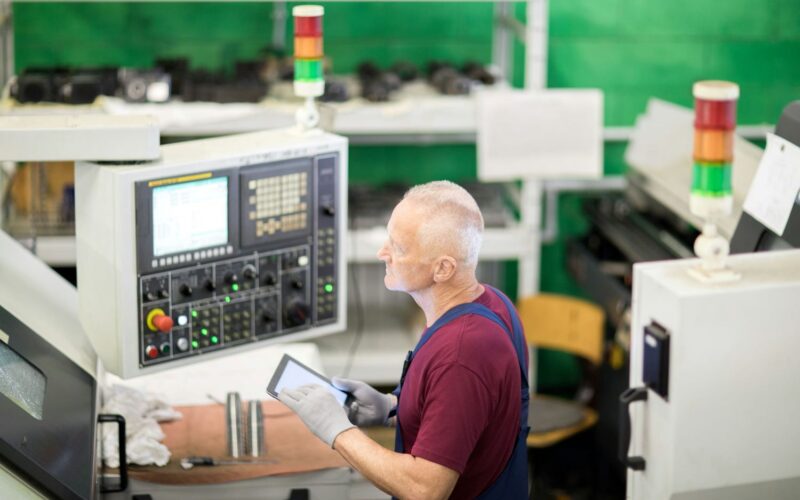 oudere man aan het werk in een fabriek met het besturen van een industrieël apparaat.
