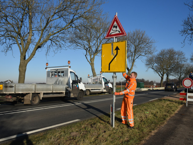 Een medewerker verkeersmaatregelen zet een bord neer voor een verkeersomleiding.