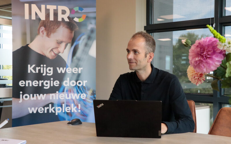 man achter laptop aan bureau zit naast een banner van intro personeel