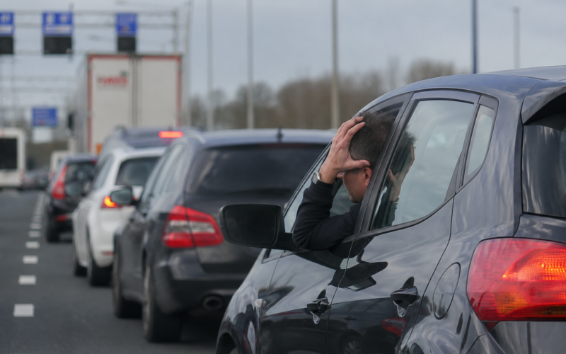 Man in a car leaning out the window, hands on head, stressed in a traffic jam on a highway