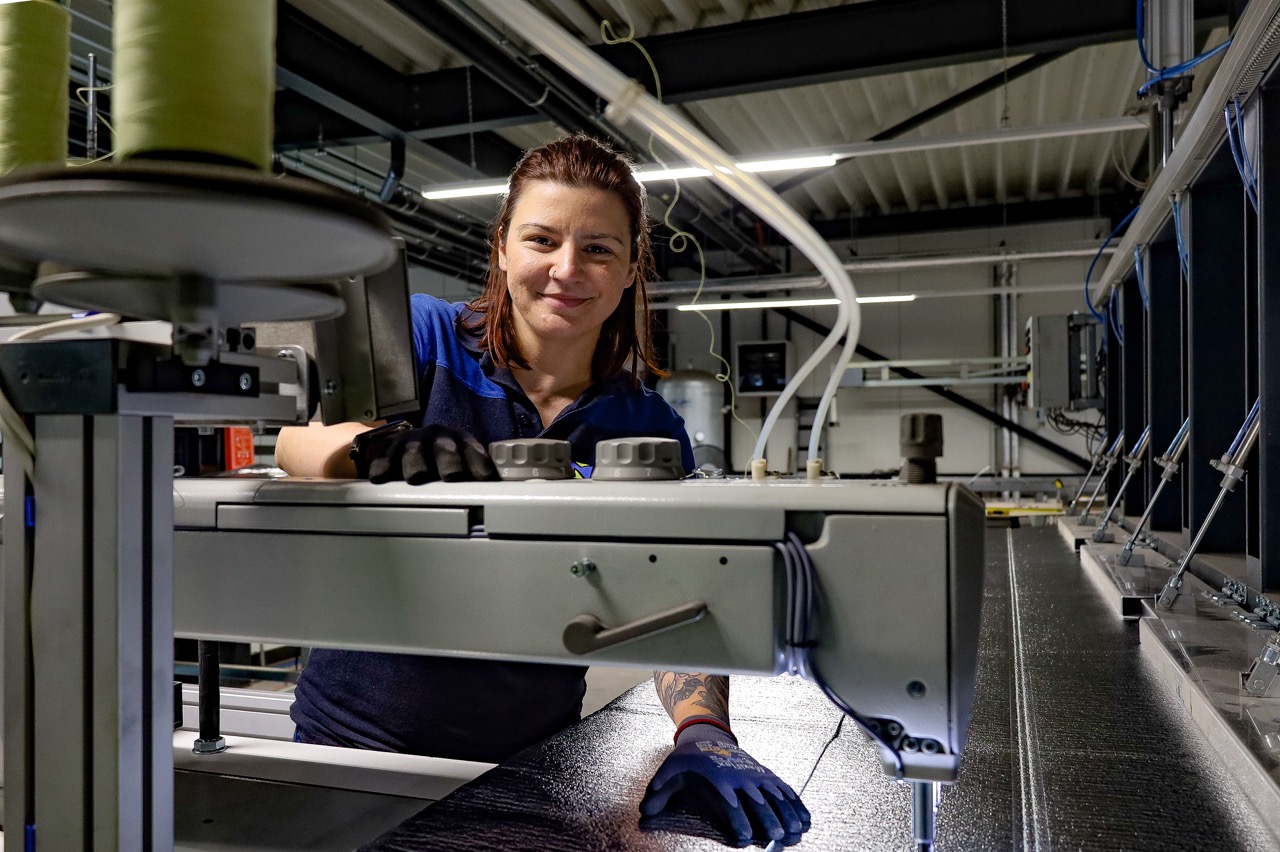 Smiling female factory worker operating a conveyor system and inspecting equipment in a manufacturing plant.