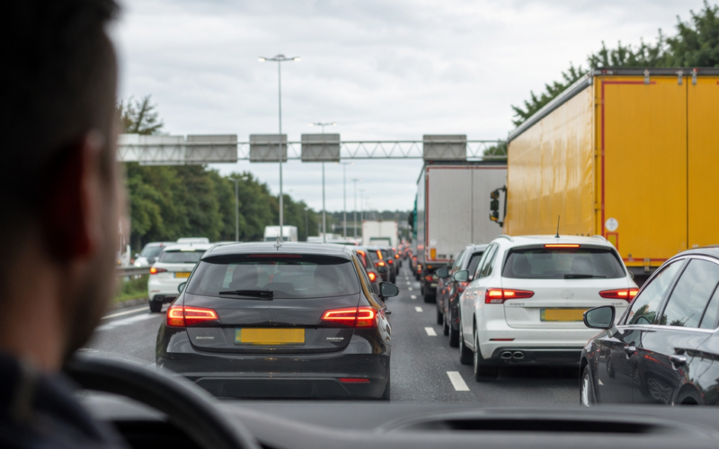 Driver’s viewpoint in a congested highway with many cars ahead and a large yellow truck to the right under a cloudy sky